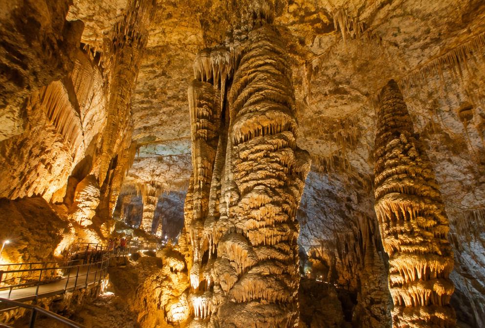 Huge illuminated limestone cave hall with towering stalagmite columns