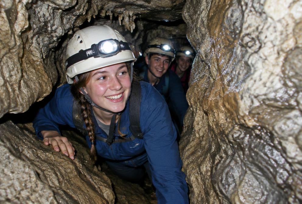 Teenagers with headlamps squeezing through a narrow cave passage