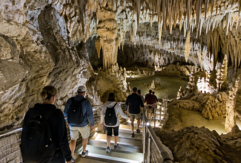 Visitors walking down lit steps into a cave chamber