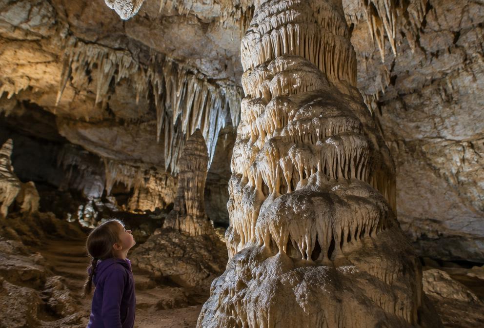 Child looking up at a giant stalagmite in a softly lit cave